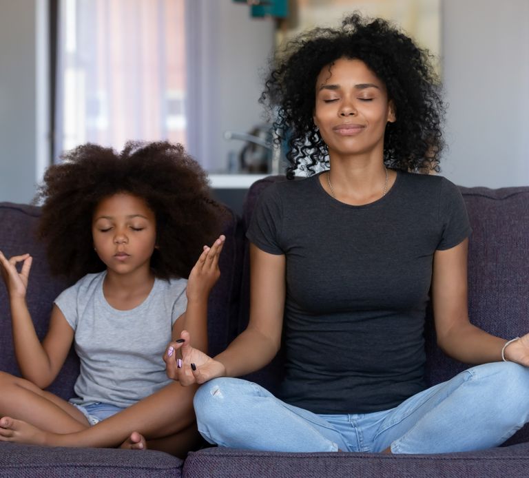 Students which looks like a parent and her child, they are practicing meditation with their legs crossed and their fingers curled on their knees